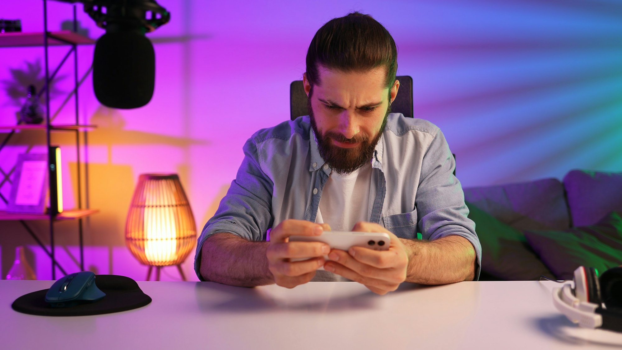 Gamer in neon room. A bearded guy sits at a table and plays a video game on his smartphone. Mobile